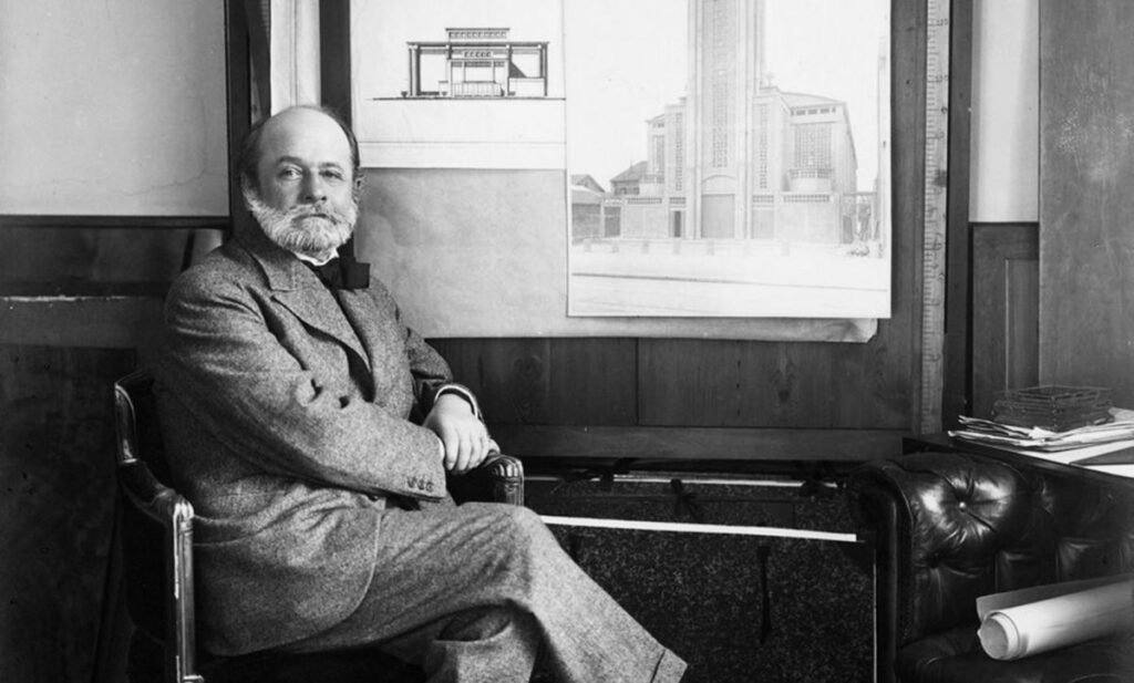 Auguste Perret posant devant des plans d'architectures papiers