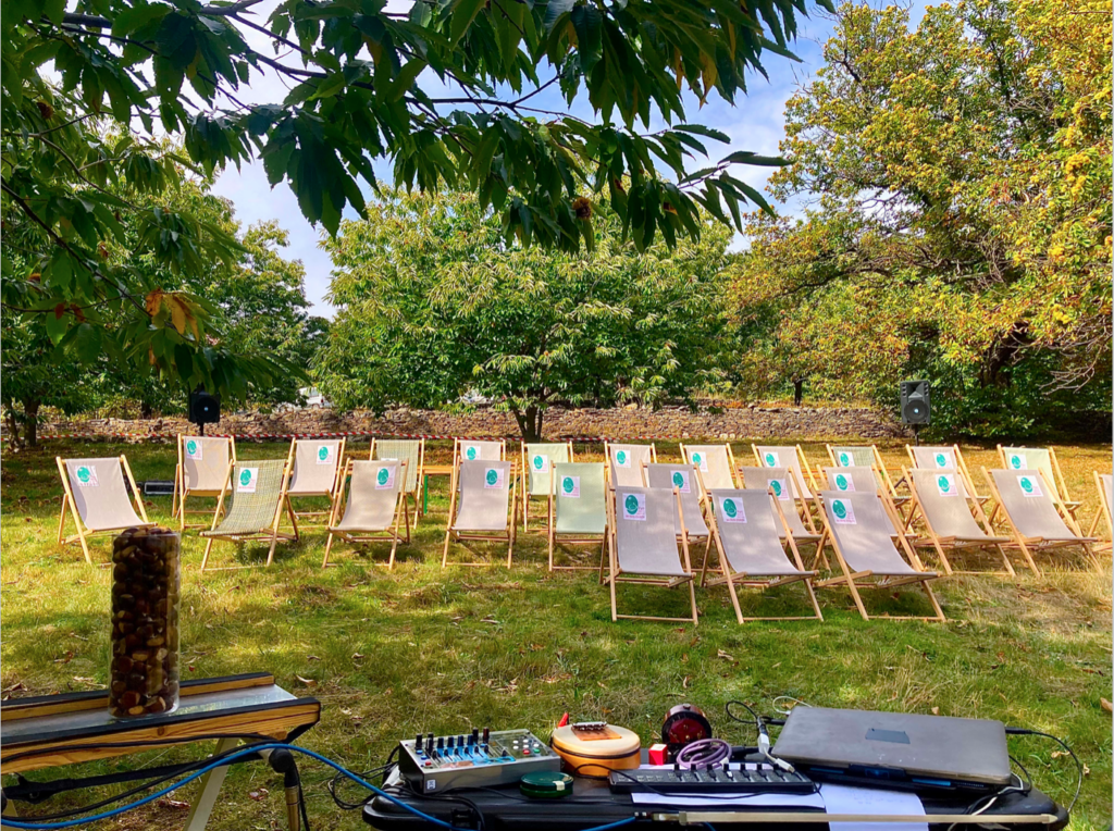 Console son et instruments installés sur une table au premier plan. Des transats disposés dans un théâtre de verdure au loin.