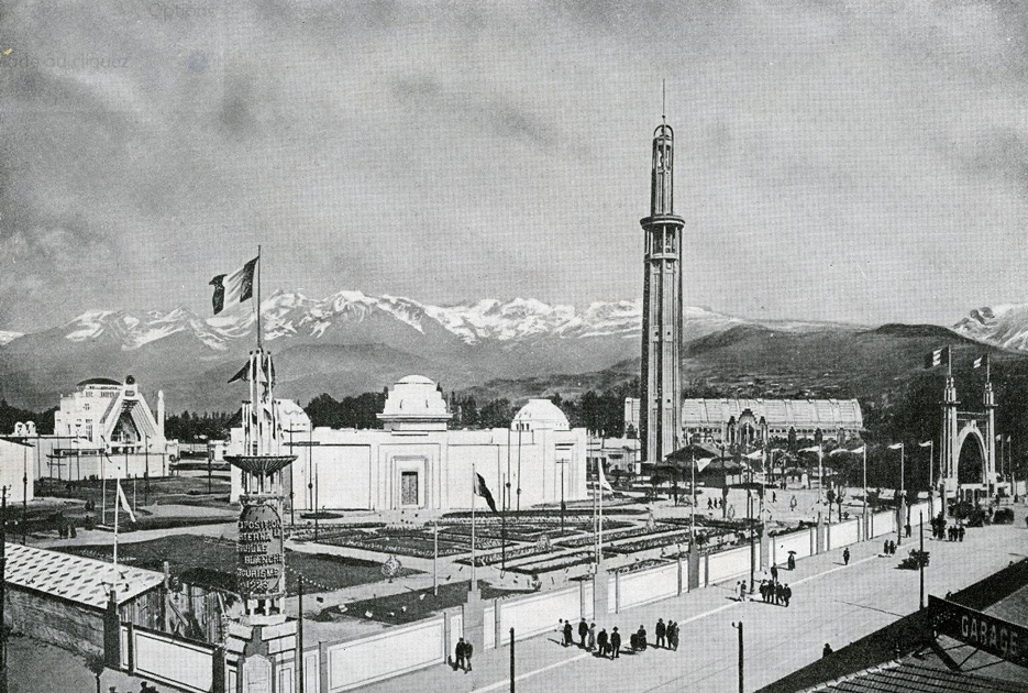 Photo en noir et blanc représentant l'exposition universelle de 1925 dont la tour Perret en premier plan et un panorama de montagnes en second plan