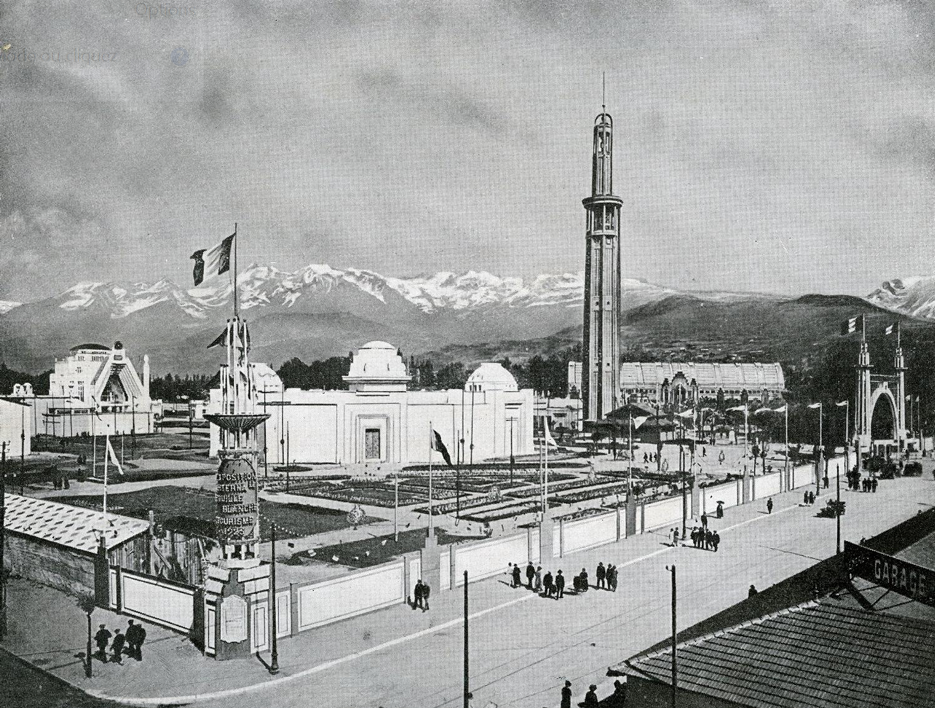 Photo en noir et blanc représentant l'exposition universelle de 1925 dont la tour Perret en premier plan et un panorama de montagnes en second plan