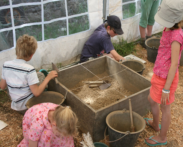quatre enfants participent à un atelier d'initiation à l'archéologie. Bac à sable et matériel professionnel
